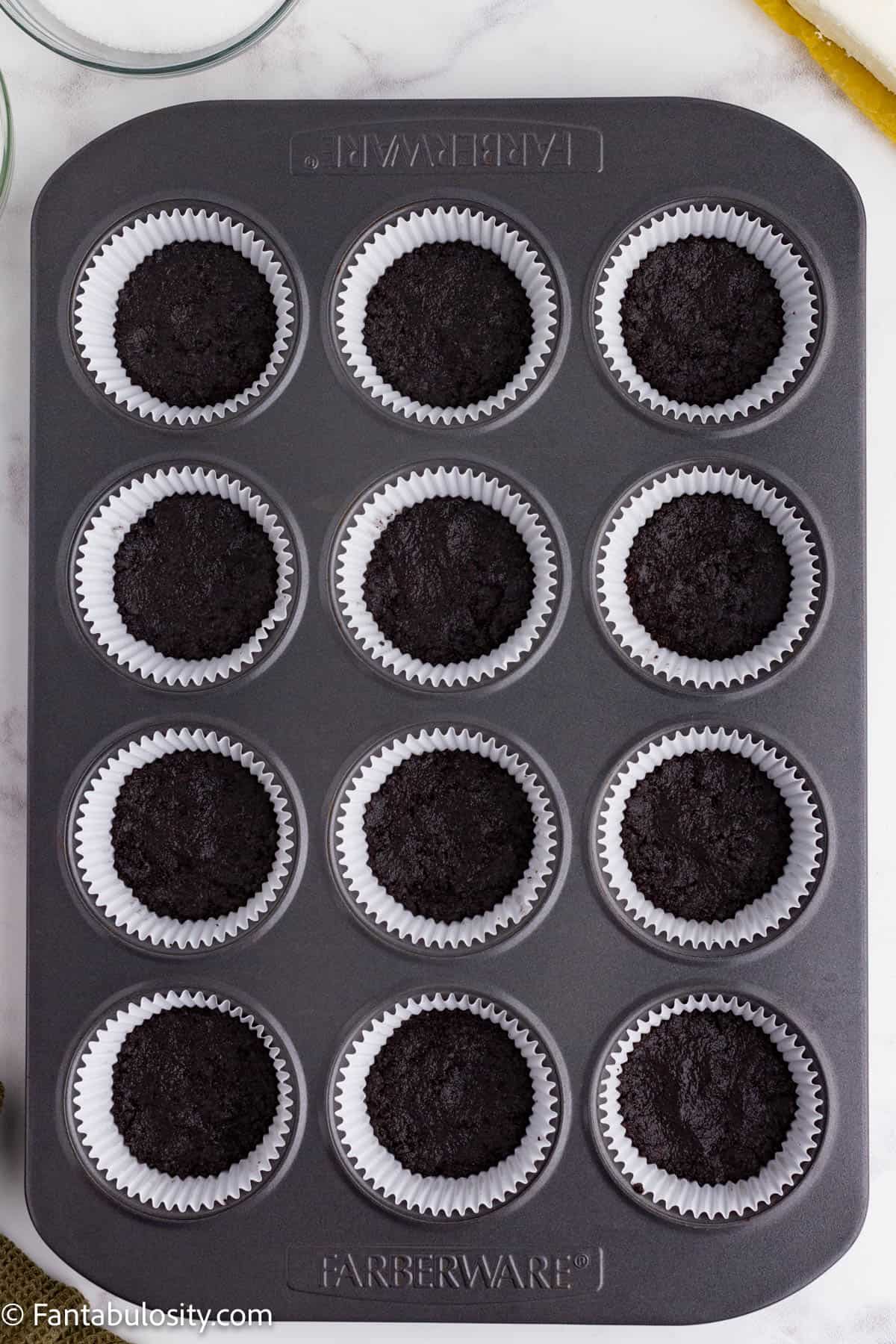 A metal cupcaketin holds 12 cupcake papers with an Oreo cookie crust pressed into the bottom