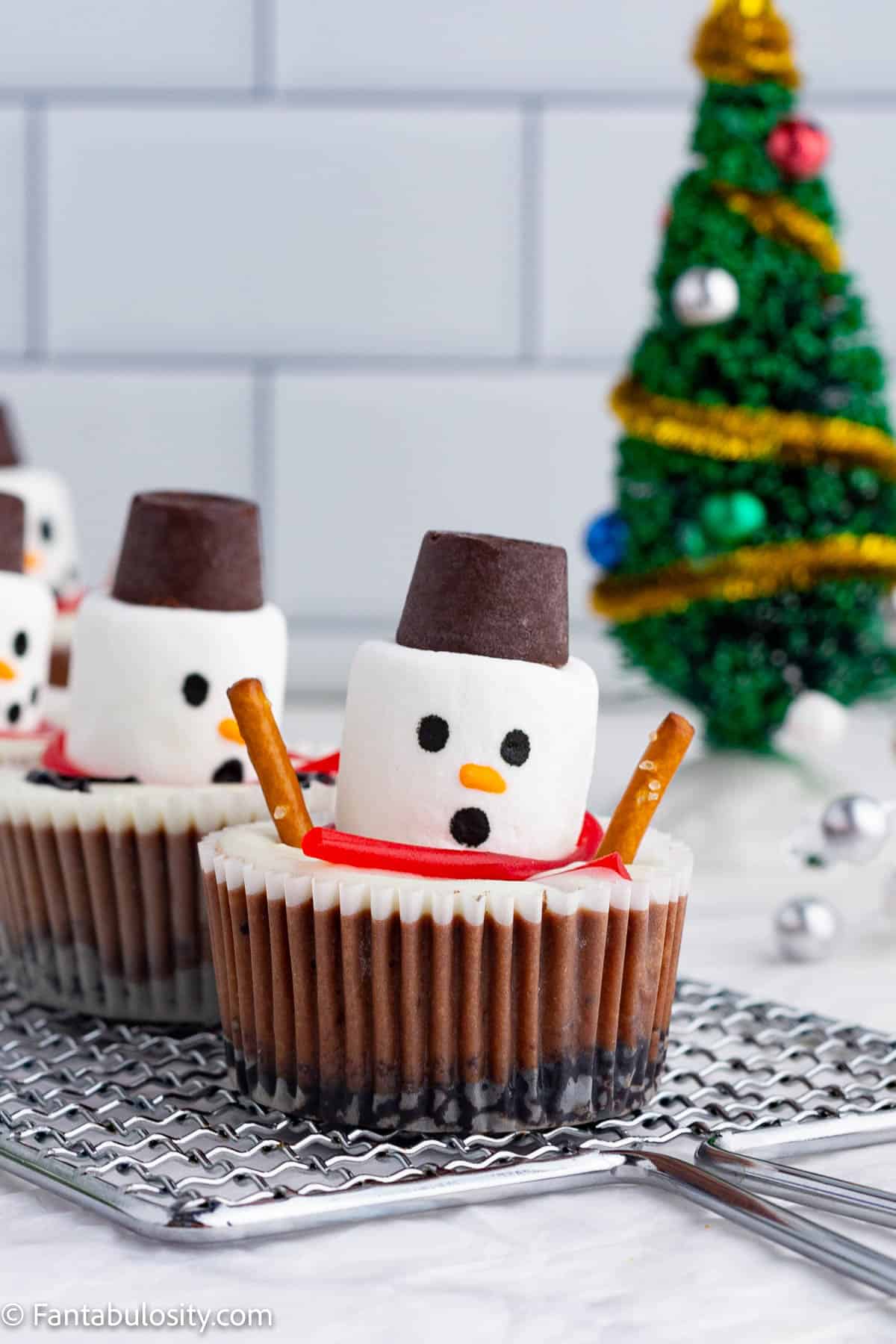 Close up photo of chocolate cheesecake cups decorated to look like melting snowmen with rolo hats, pretzel arms, licorice scarves and surprised faces