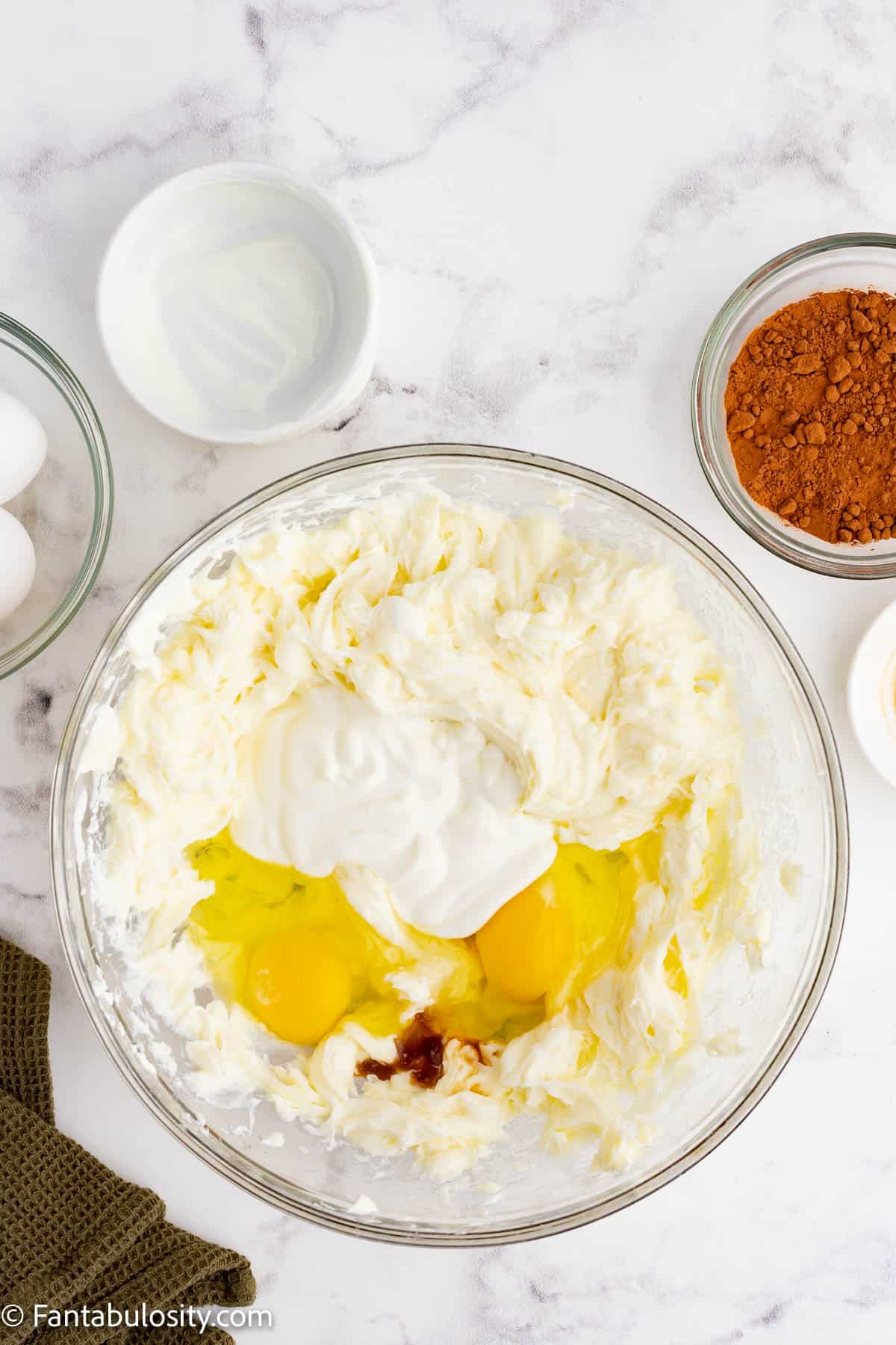 Eggs, sour cream and vanilla extract have been added to a cream cheese mixture in a large glass mixing bowl