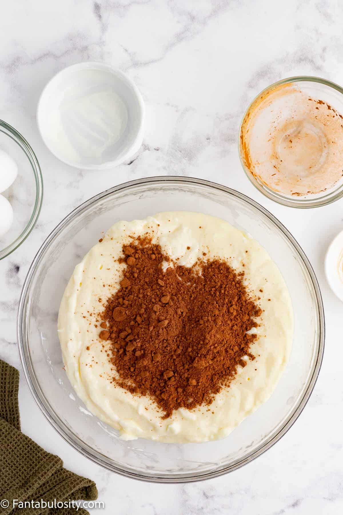 Cocoa powder has been added to a cheesecake filling in a glass mixing bowl