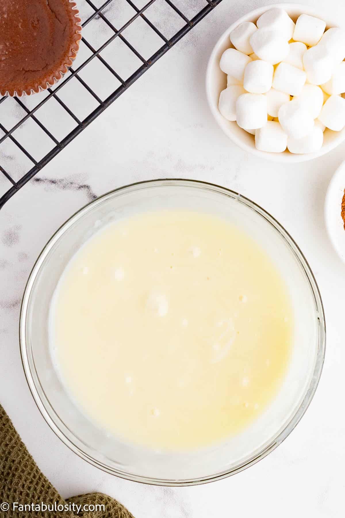 A glass mixing bowl holds creamy white chocolate ganache