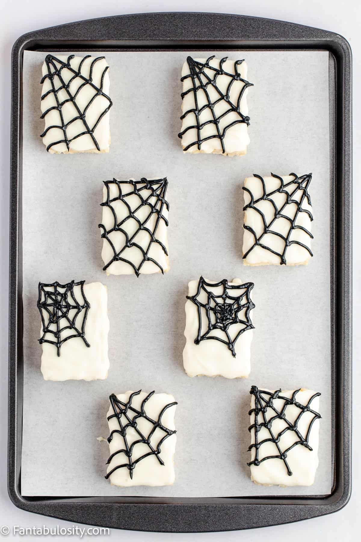Chocolate covered Rice krispie treats are decorated with black piped spider webs and laid on a parchment lined baking sheet