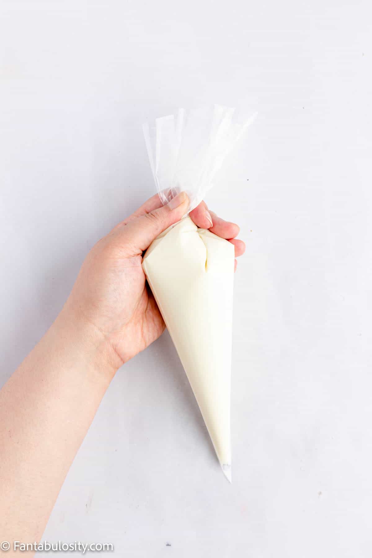 A hand is holding a piping bag that is filled with melted white chocolate