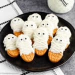Nutter Butter Mummies Cookies are displayed on a black plate on a decorative white & black cloth in the center of the photo