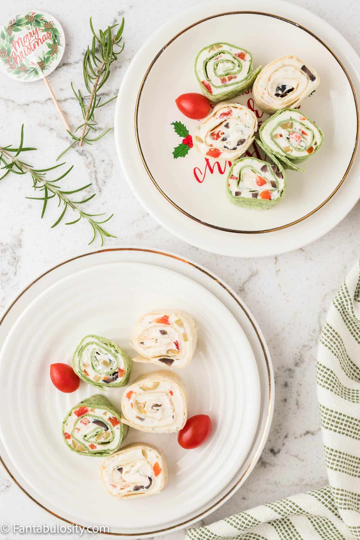 Slices of rolled tortilla pinwheels are served on two white plates, you can see the cream cheese filling studded with olives and pimientos
