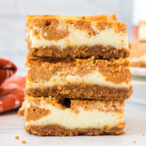 A stack of desserts bars with a graham cracker crust and swirled pumpkin cheesecake filling are in the center of the photo