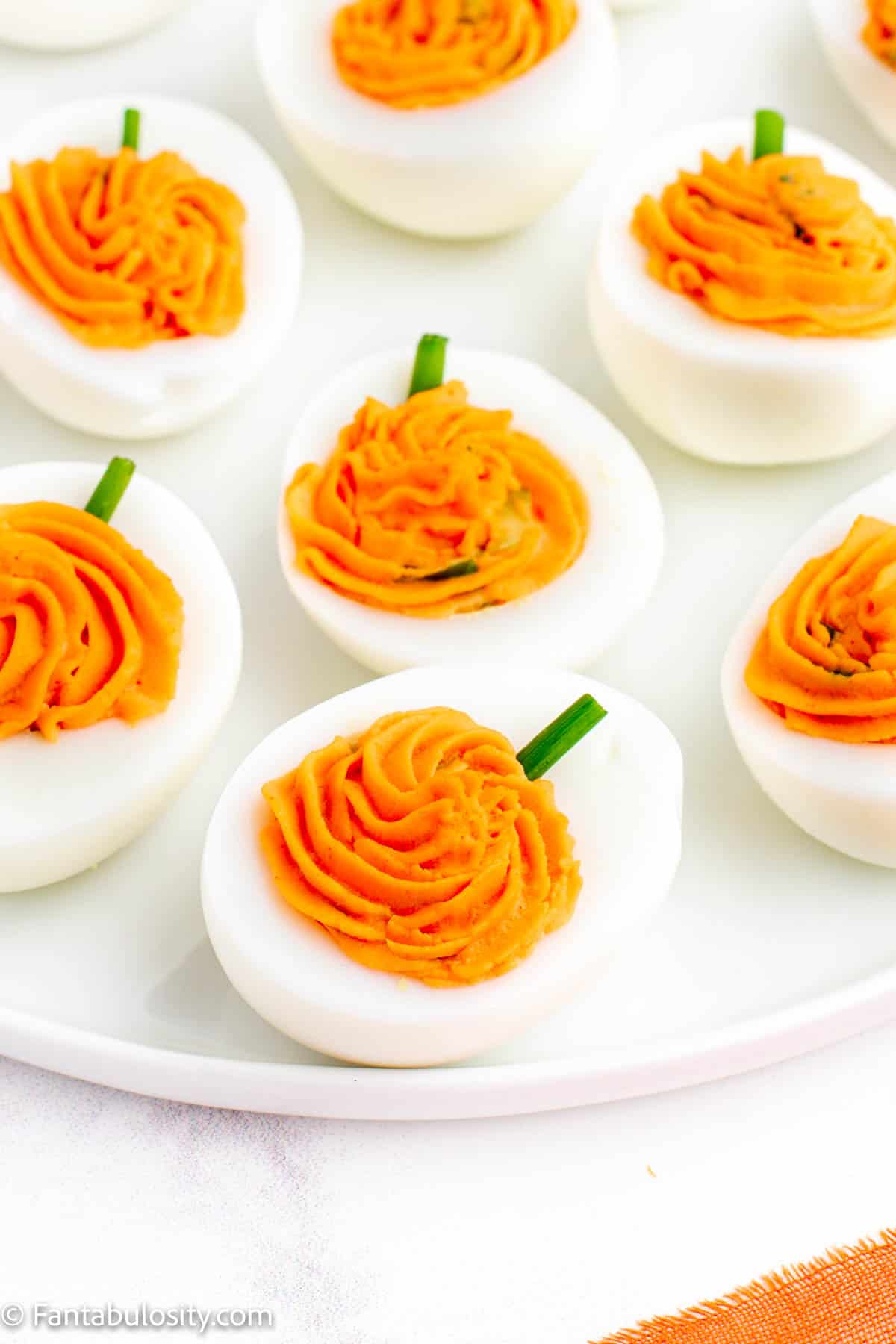 A close up of halved hard boiled eggs filled with orange yolk filling and snipped chives inserted as stems to look like pumpkins