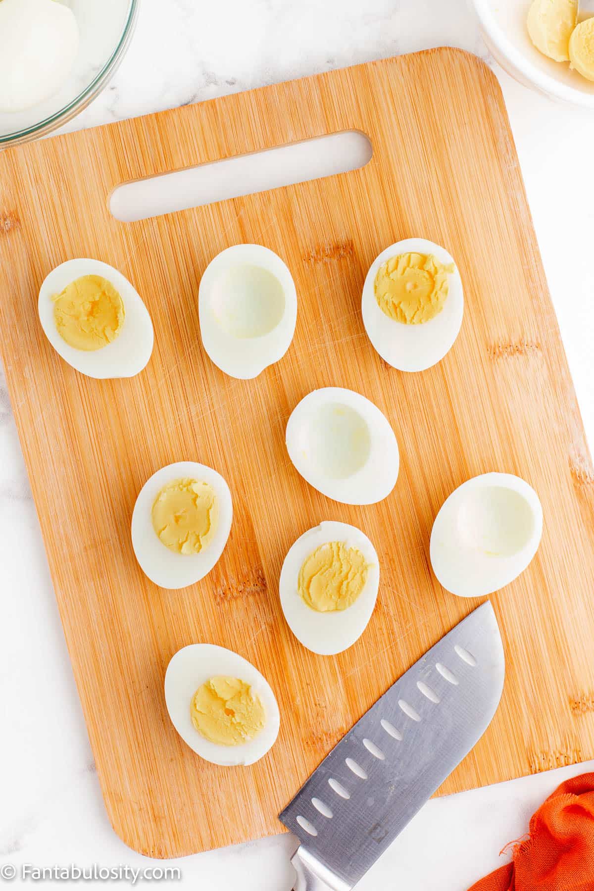 A wooden cutting board displays halved hard boiled eggs, some with the yolks removed