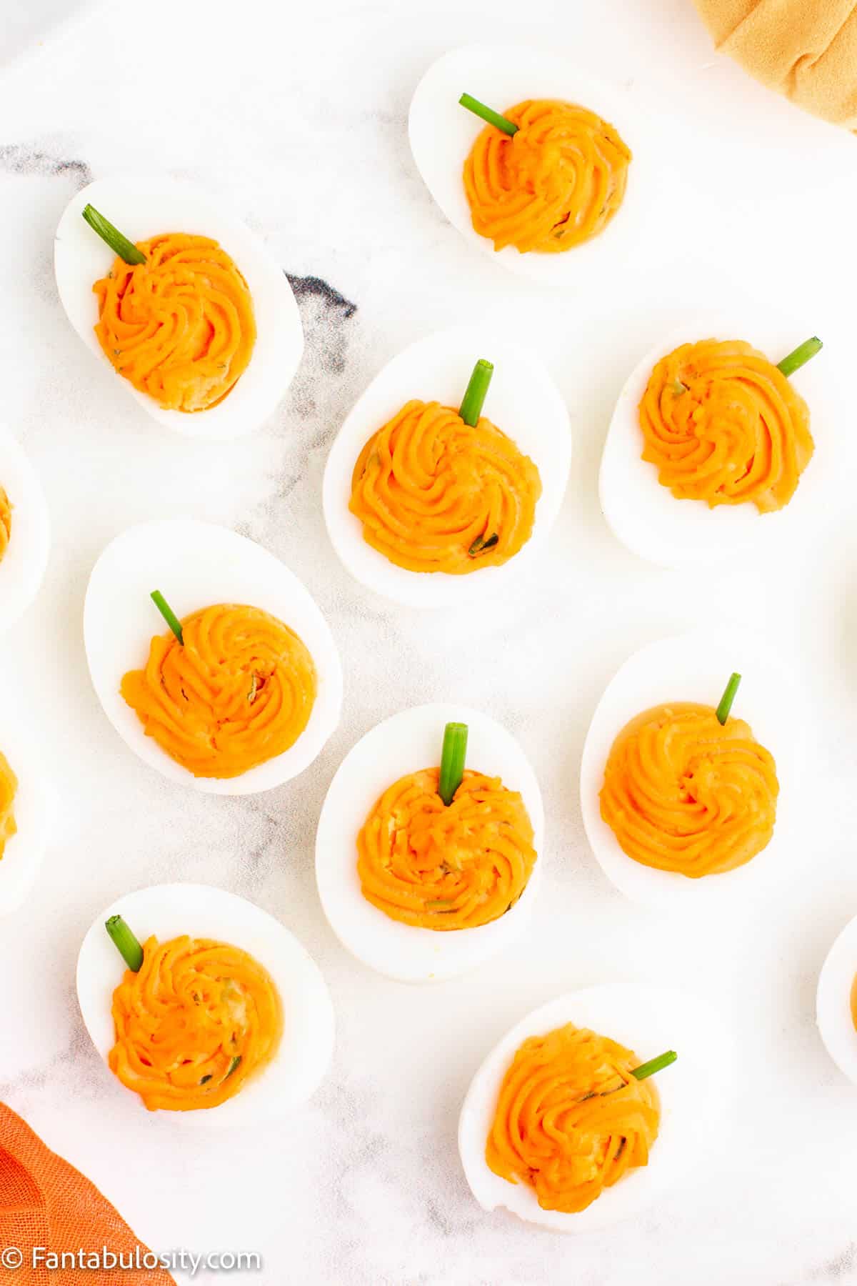Hard boiled eggs halves filled to look like pumpkins are sitting on a white marble background
