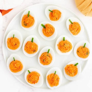A round white plate is filled with halved hard boiled eggs with orange yolk filling piped to look like a pumpkin