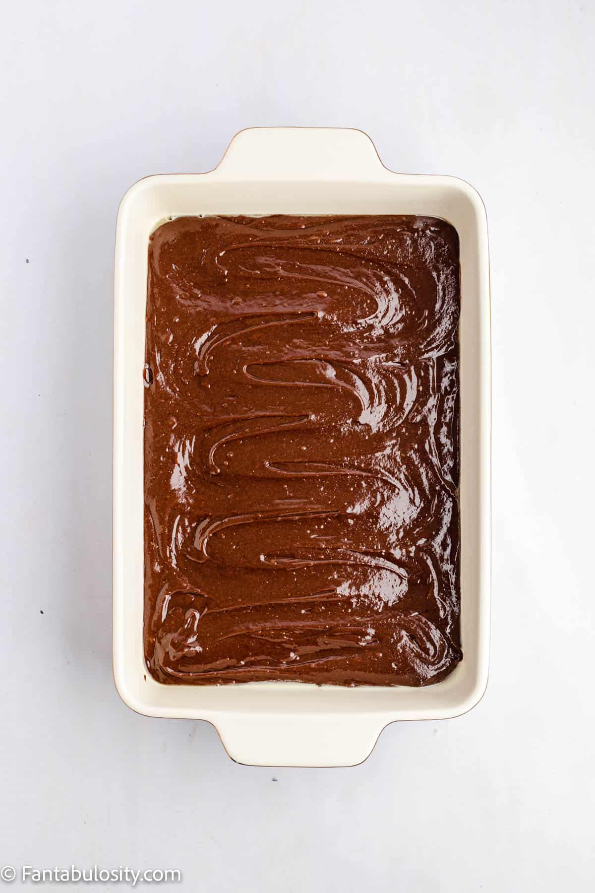 A simple photo with a pan of brownie batter spread in a white 9 inch by 13 inch baking dish