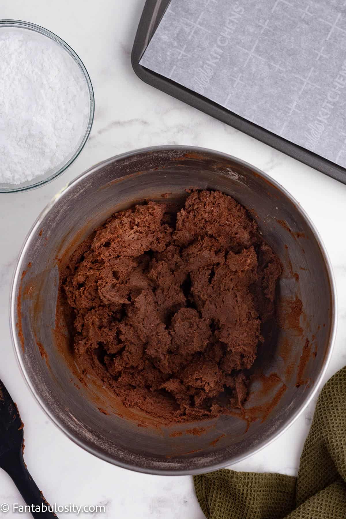 Deep brown chocolate cookie dough is shown in a large metal mixing bowl