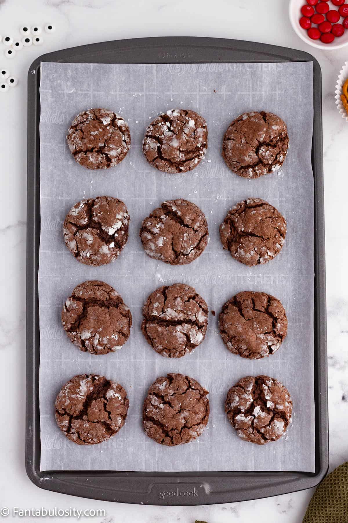 A metal baking sheet lined with parchment paper holds 12 baked chocolate cookies