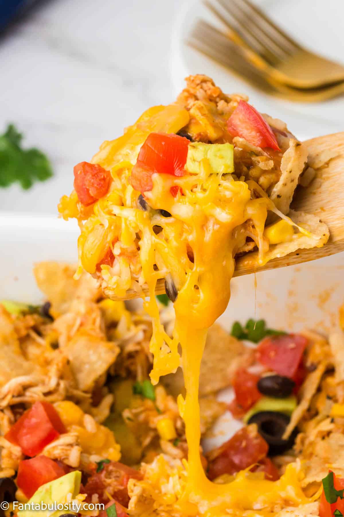 A wood spoon scooping taco chicken casserole out of the casserole dish. You can see that the cheese is melted and stringy.