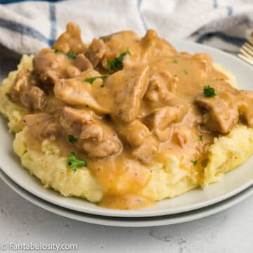 Chicken and gravy on top of mashed potatoes on white plates