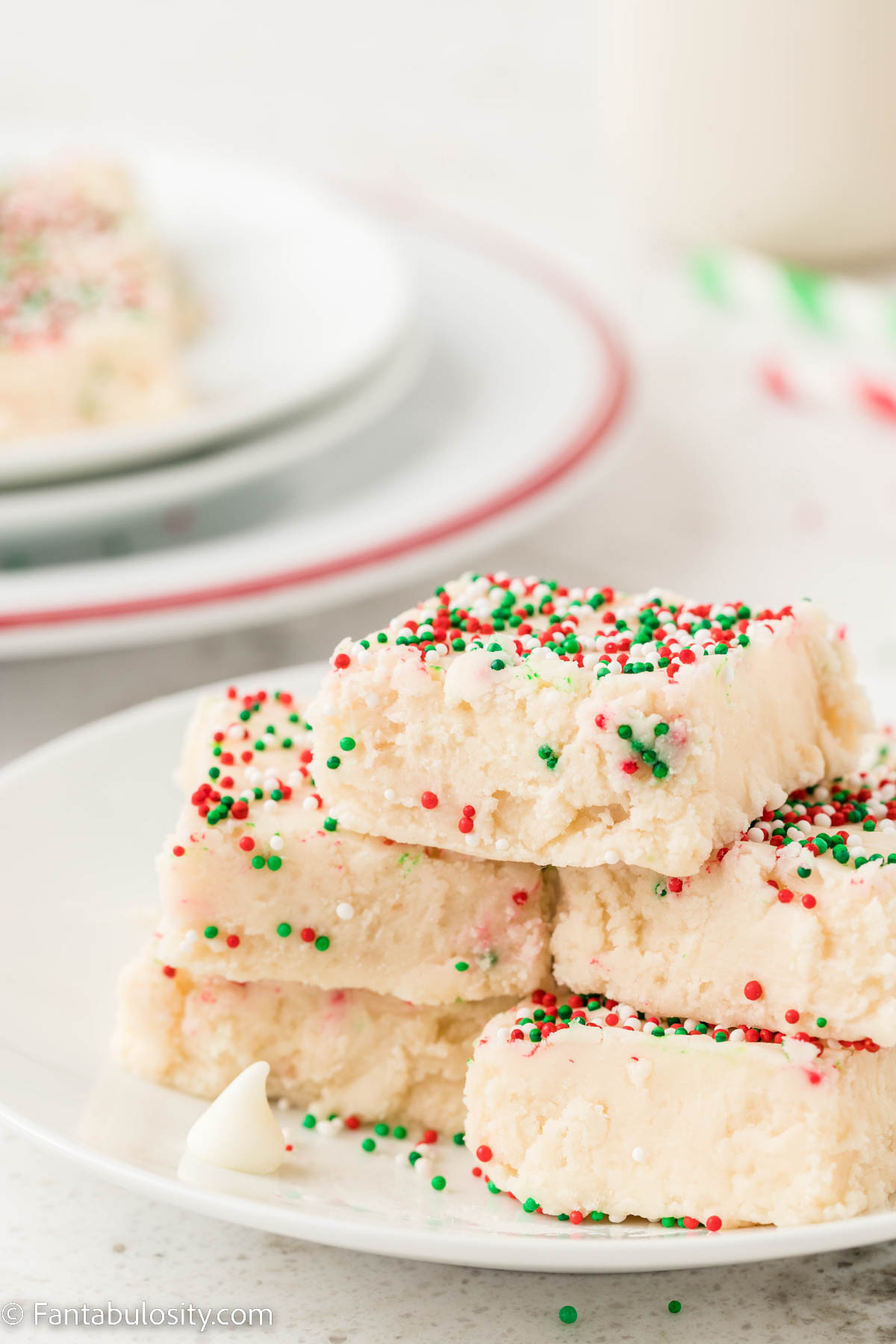 A white plate holding pieces of white fudge topped with red, white and green sprinkles is in the center of the photo
