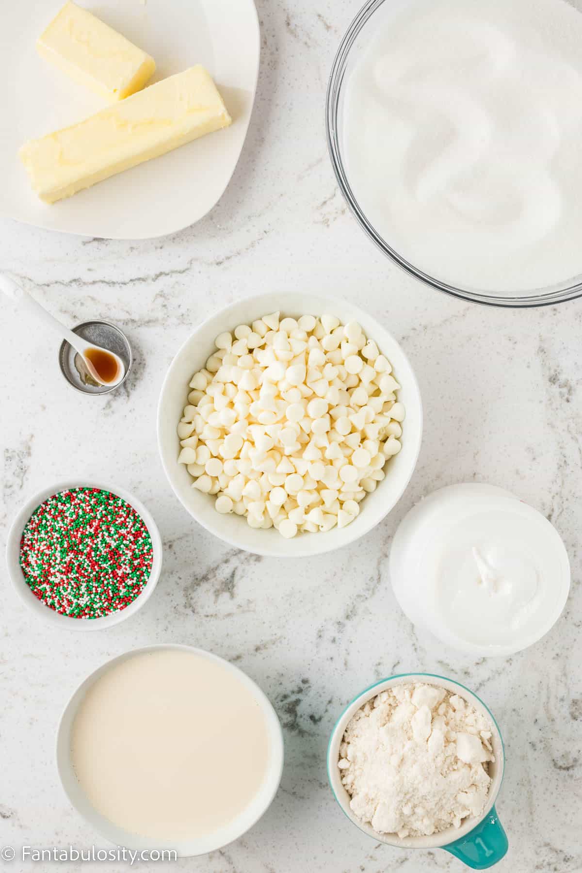 Bowls of ingredients to make Christmas cookie fudge are displayed on a white marble background