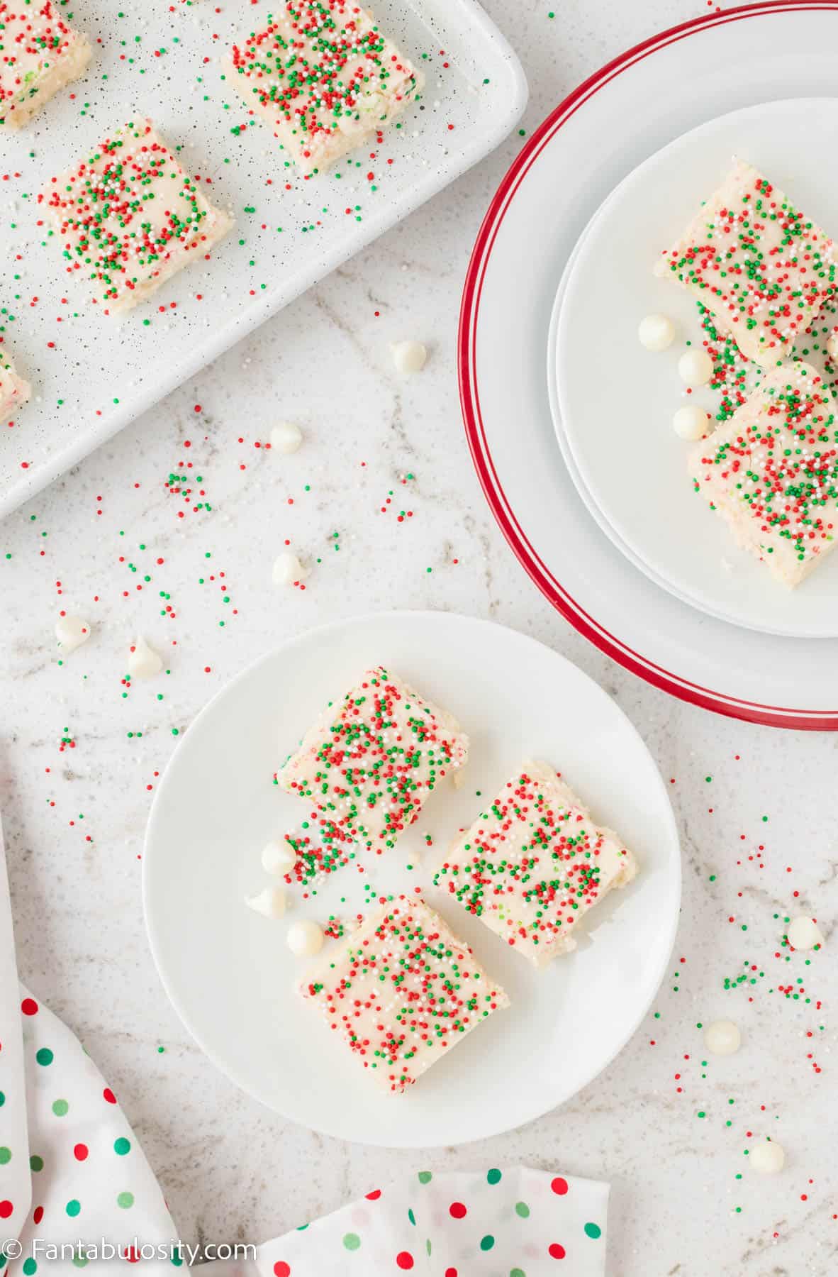 A birdseye photo of several plates holding pieces of white chocolate fudge with red white and green sprinkles