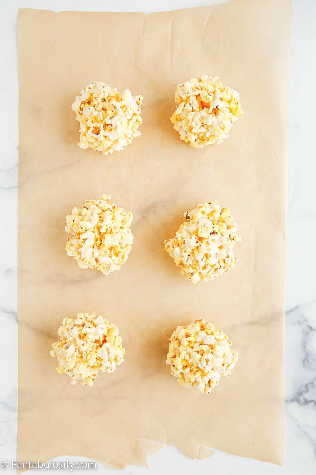 6 round marshmallow popcorn balls have been placed on a piece of parchment paper