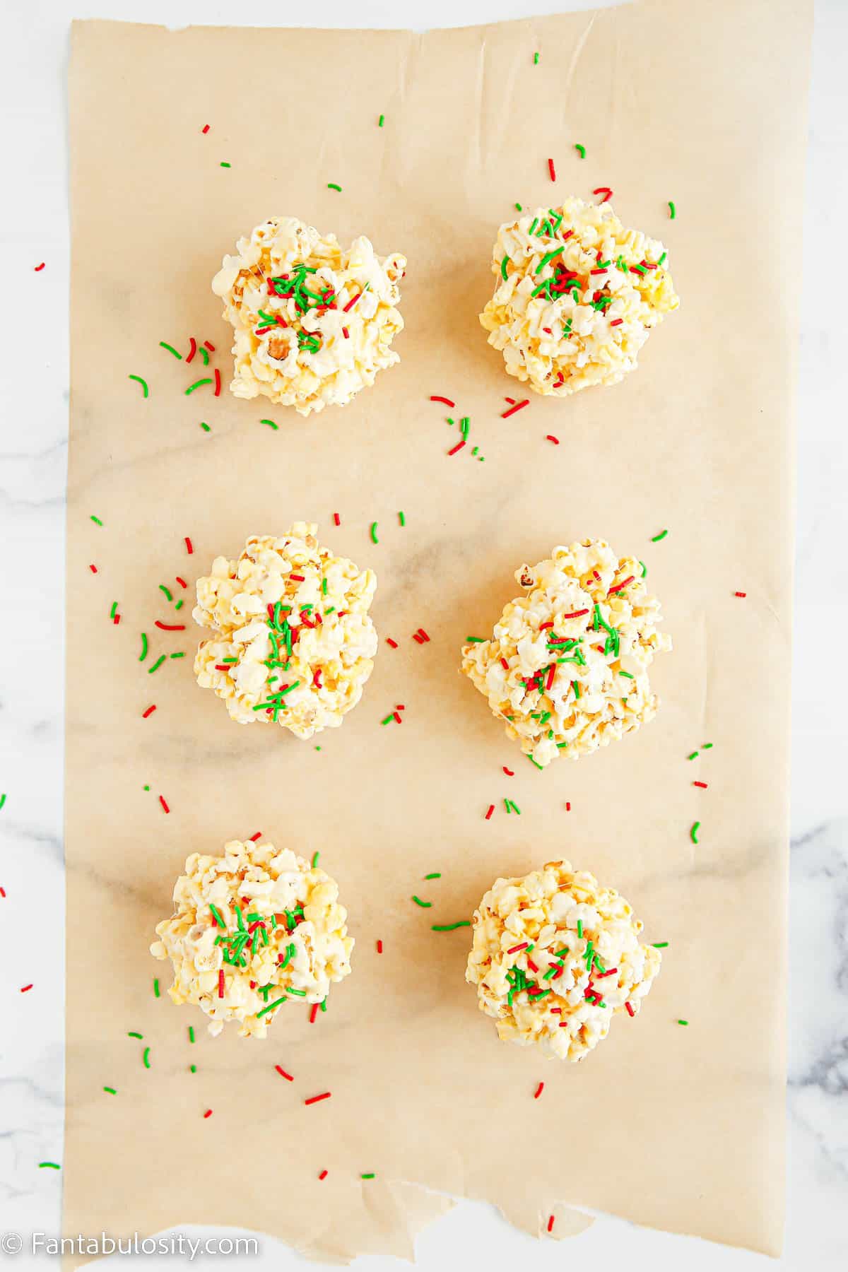 6 marshmallow popcorn balls have been sprinkled with red and green jimmies