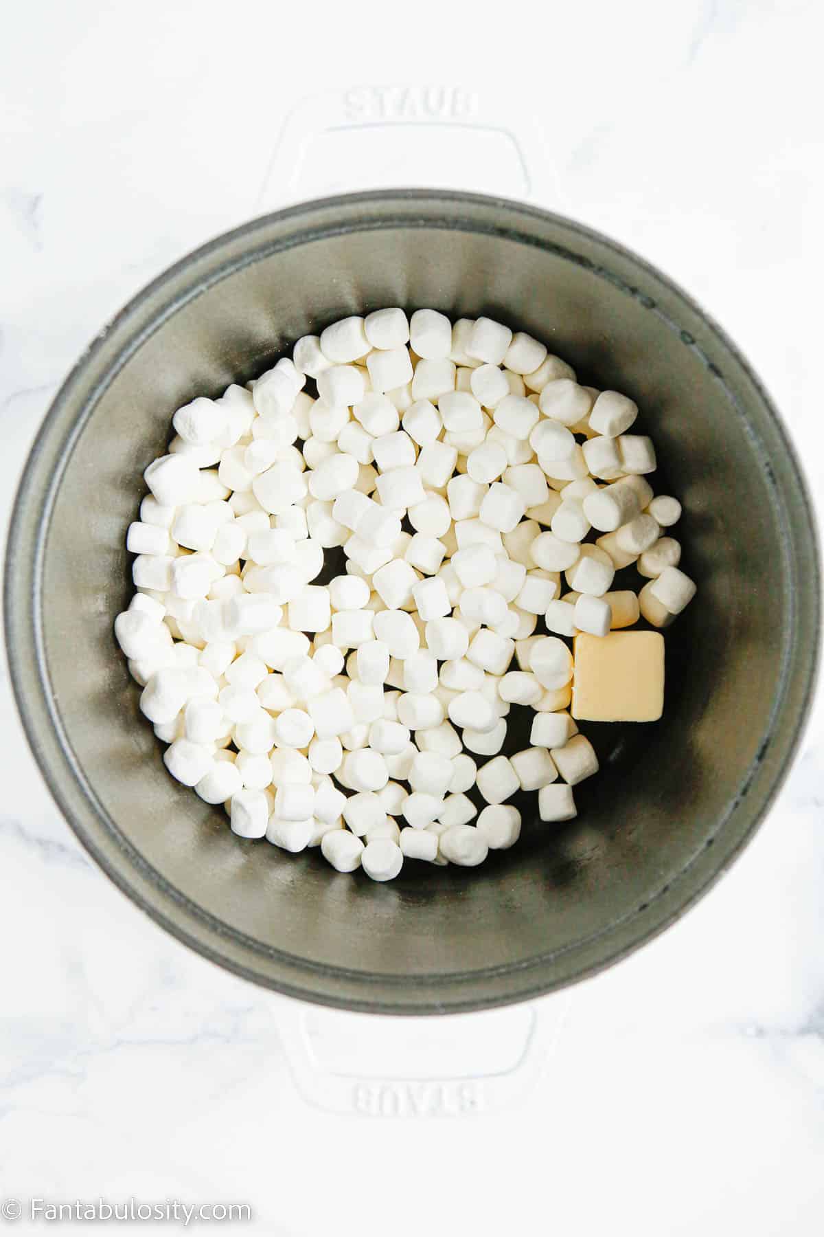 A white dutch oven holds mini marshmallows and a pat of butter
