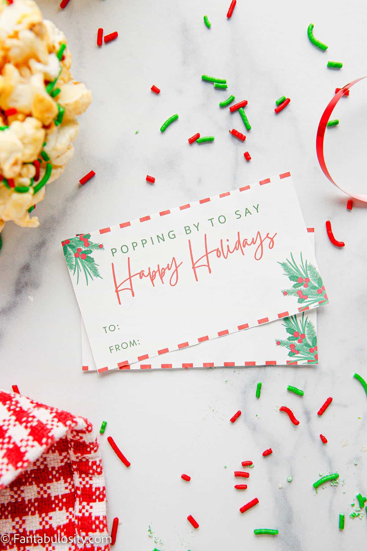 Gift tags that read "Popping By to say Happy Holidays" are displayed on a white marble background surrounded with colorful Christmas colored sprinkles