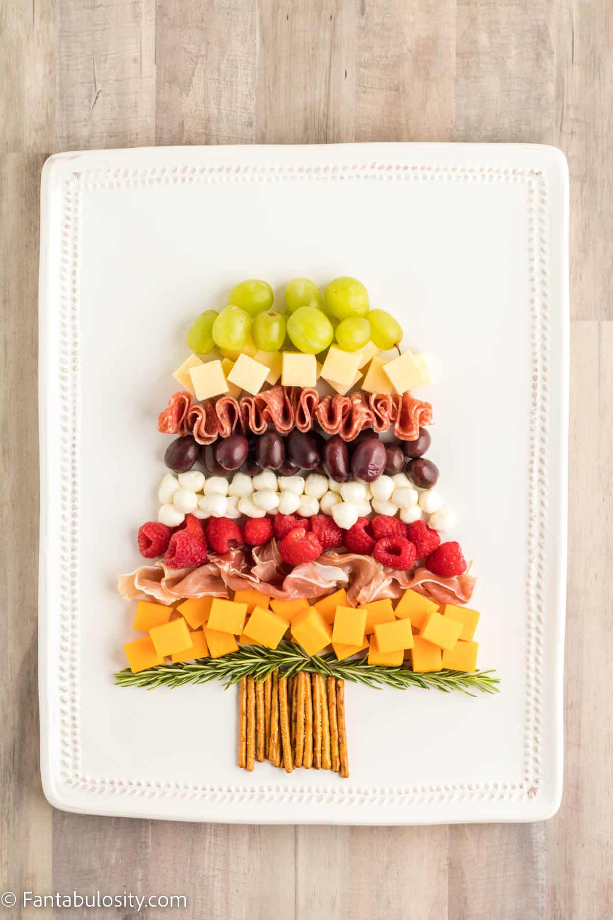A row of green grapes has been added to continue creating the shape of a Christmas tree on a rectangular white platter