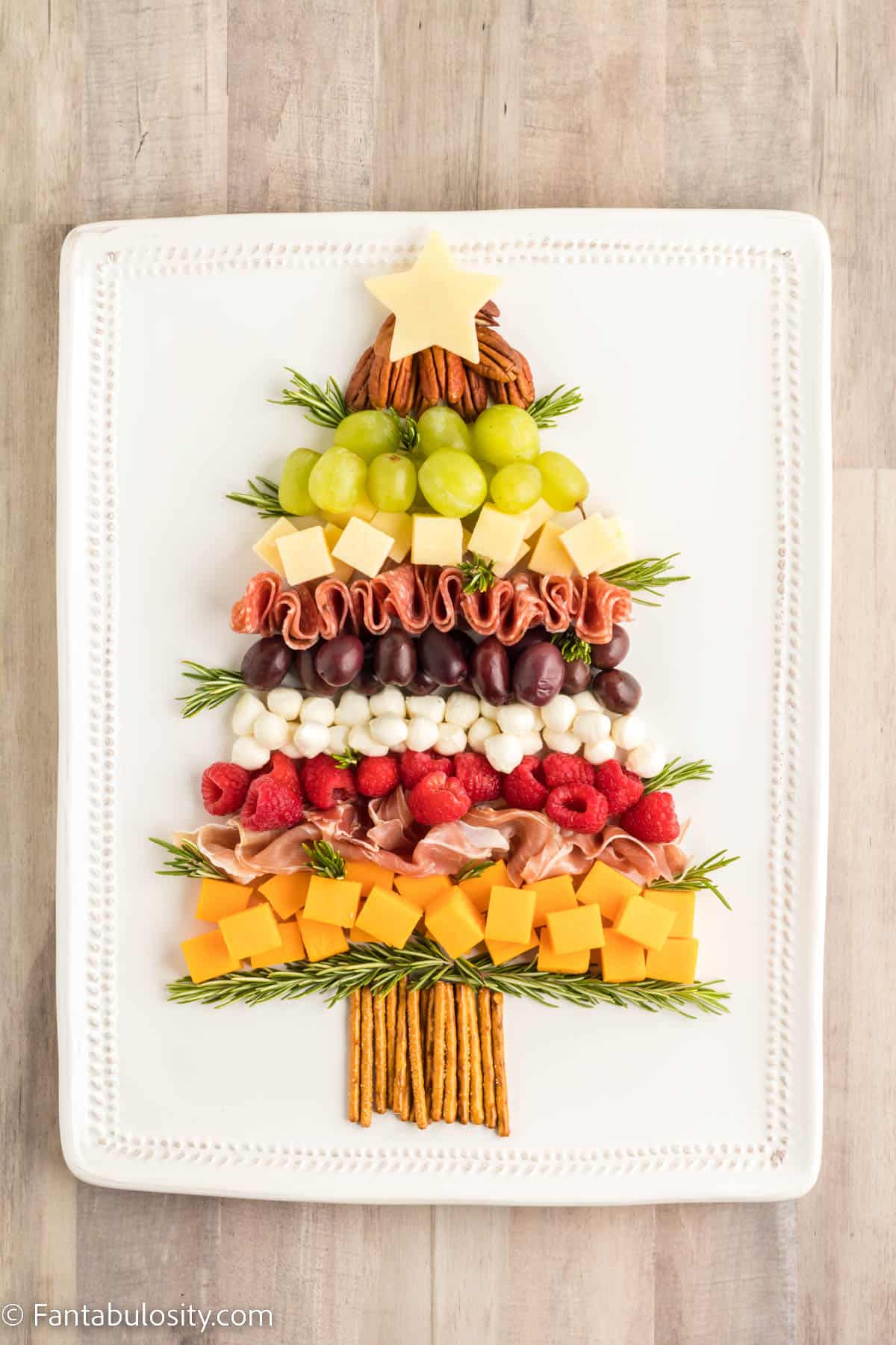 Additional sprigs of fresh rosemary have been tucked into the fruit, nuts, meats and cheese of a Christmas tree shaped platter of charcuterie