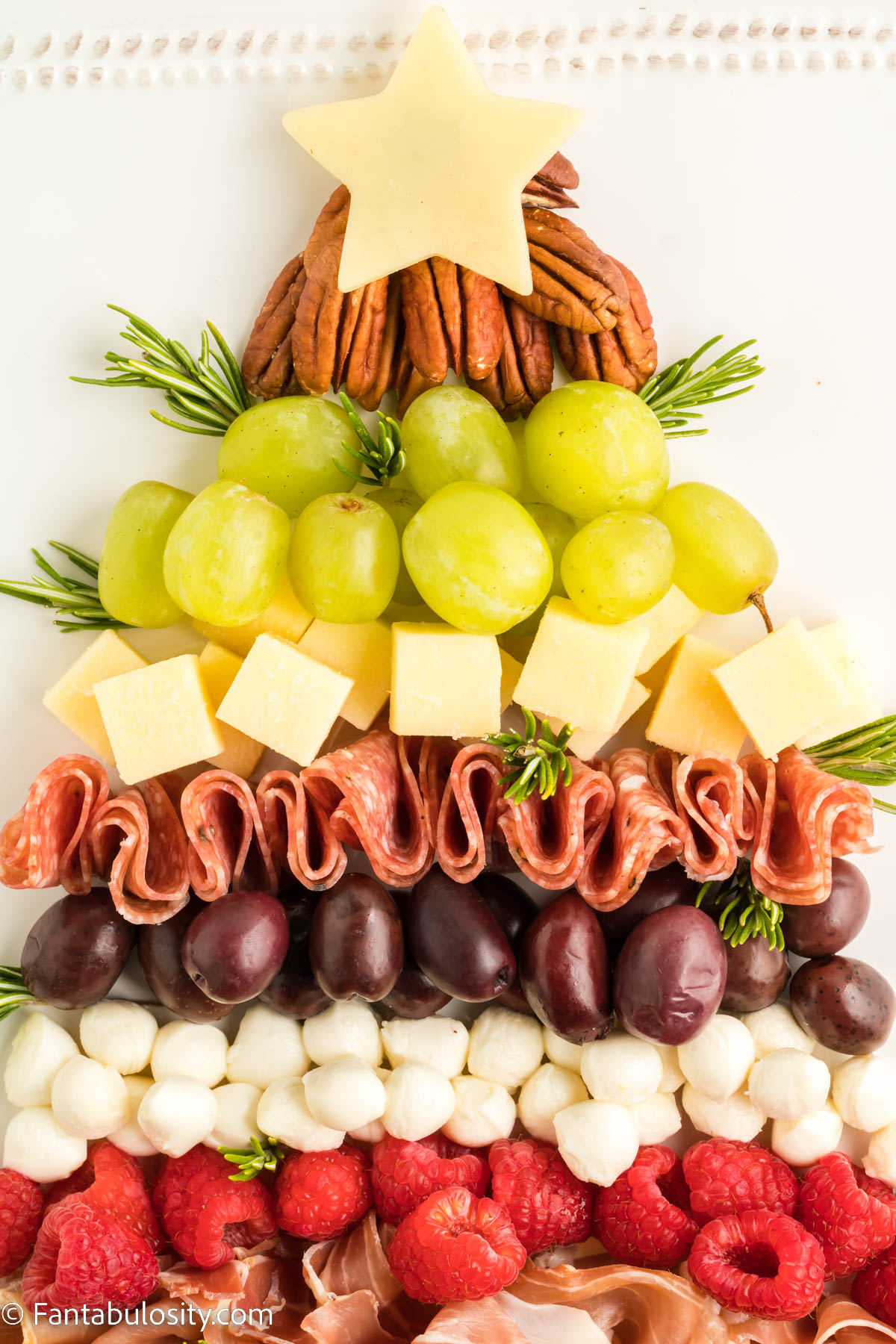 Close up photo of meat, cheese, fruit and nuts that has been arranged in the shape of a Christmas tree with a star shaped piece of cheese at the top