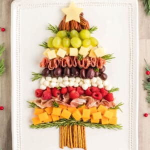 A rectangular white platter holds charcuterie in the shape of a Christmas tree