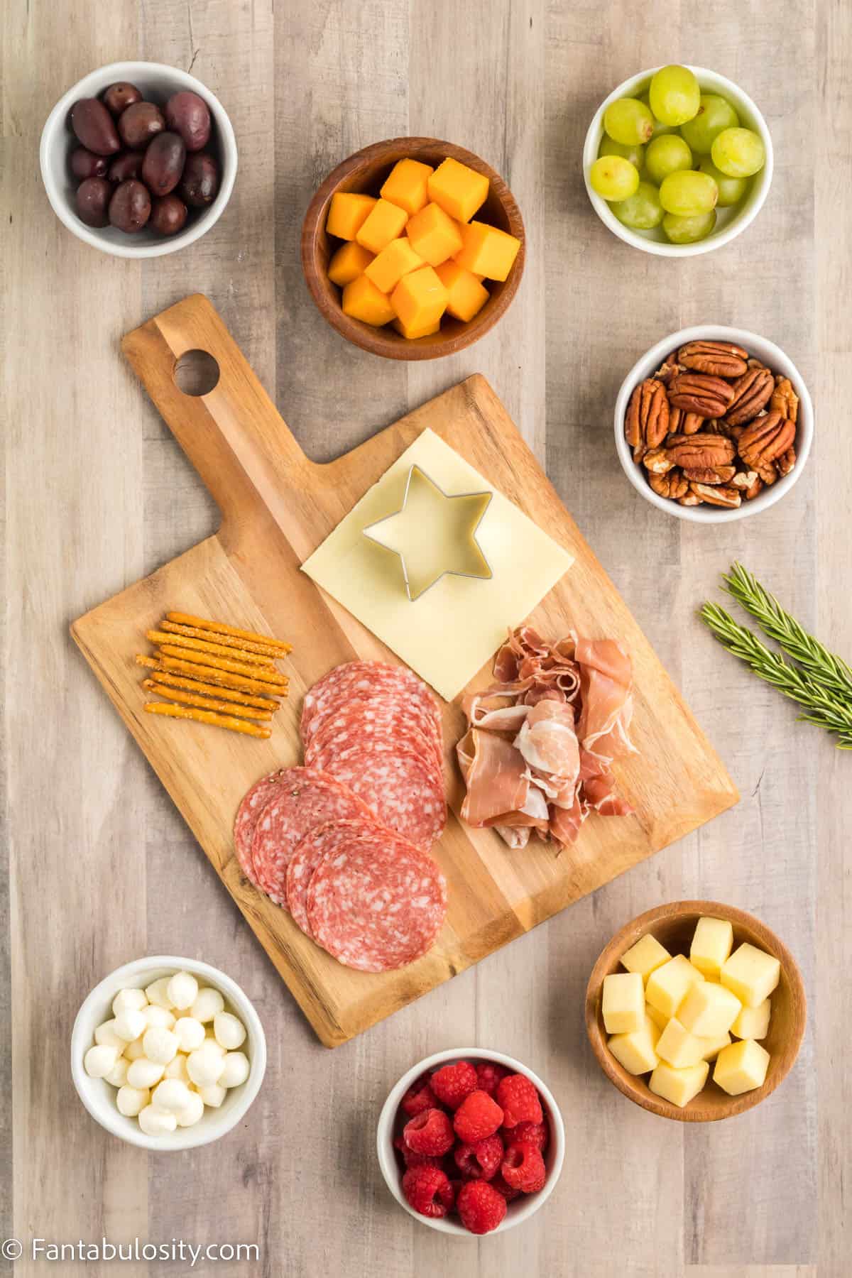 Bowls fruit, cheese and nuts and a wooden board holding different types of meat are displayed