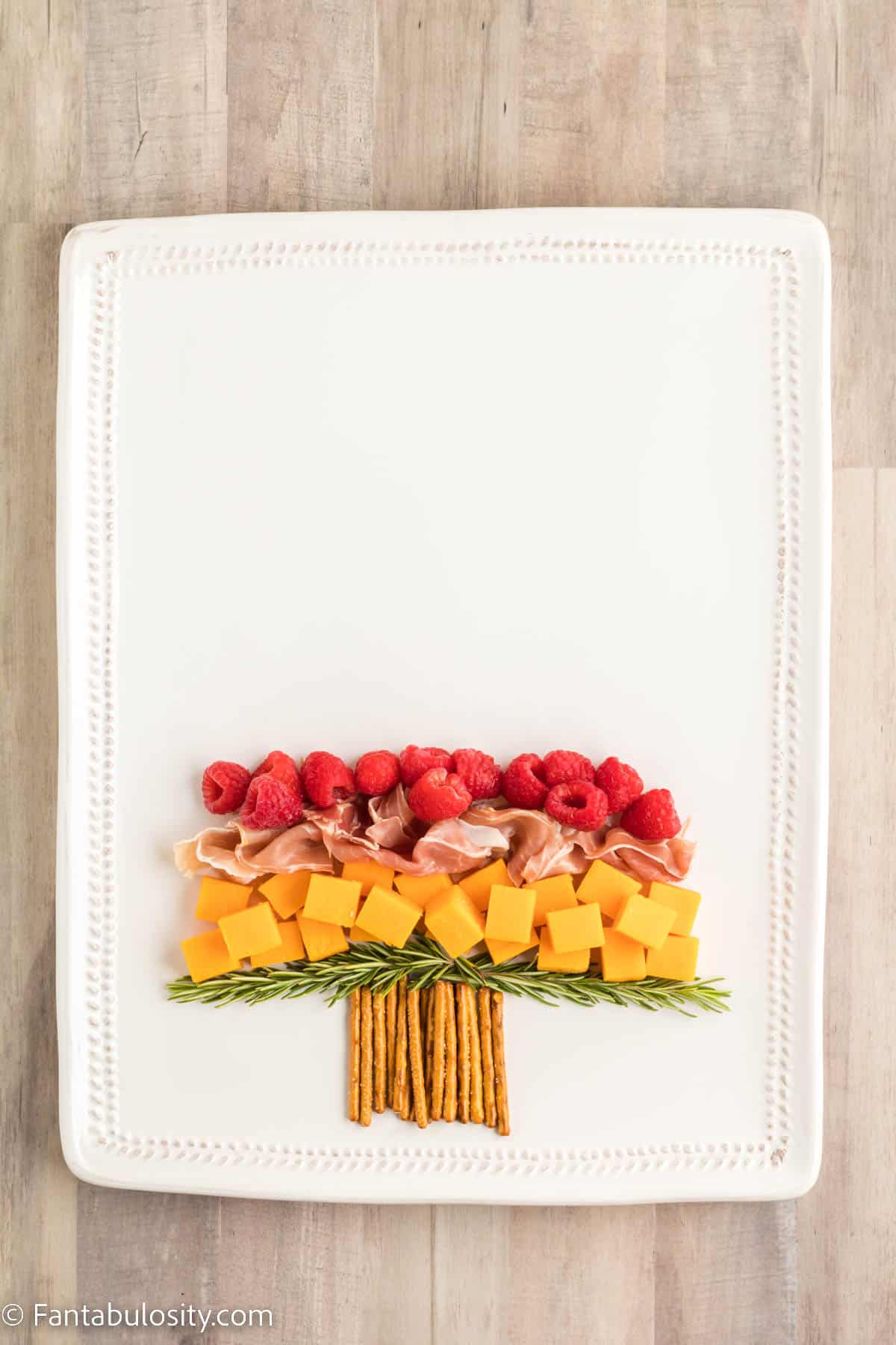 A row of bright red raspberries have been added to continue creating the shape of a Christmas tree on a rectangular white platter