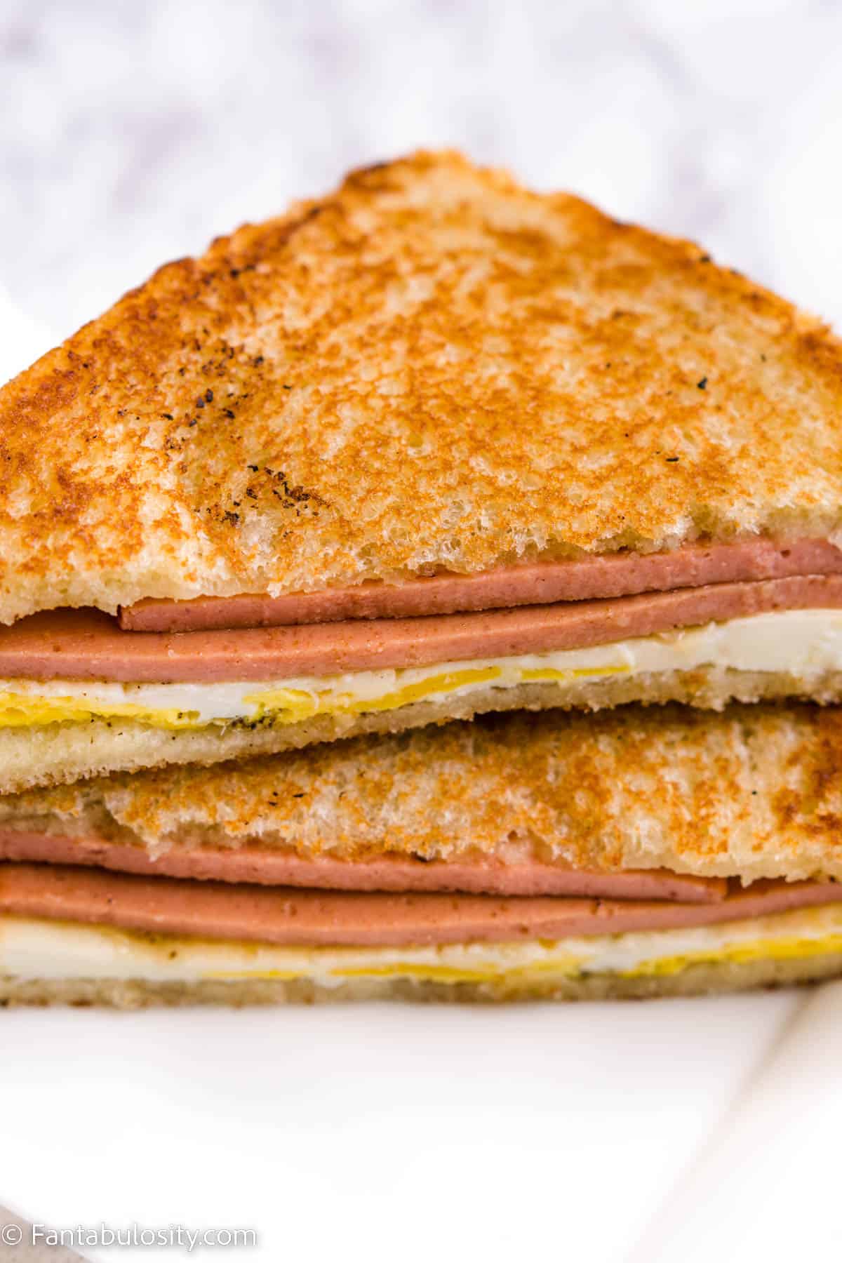 Fried Bologna and Egg Sandwich, cut in half, sitting on white plate