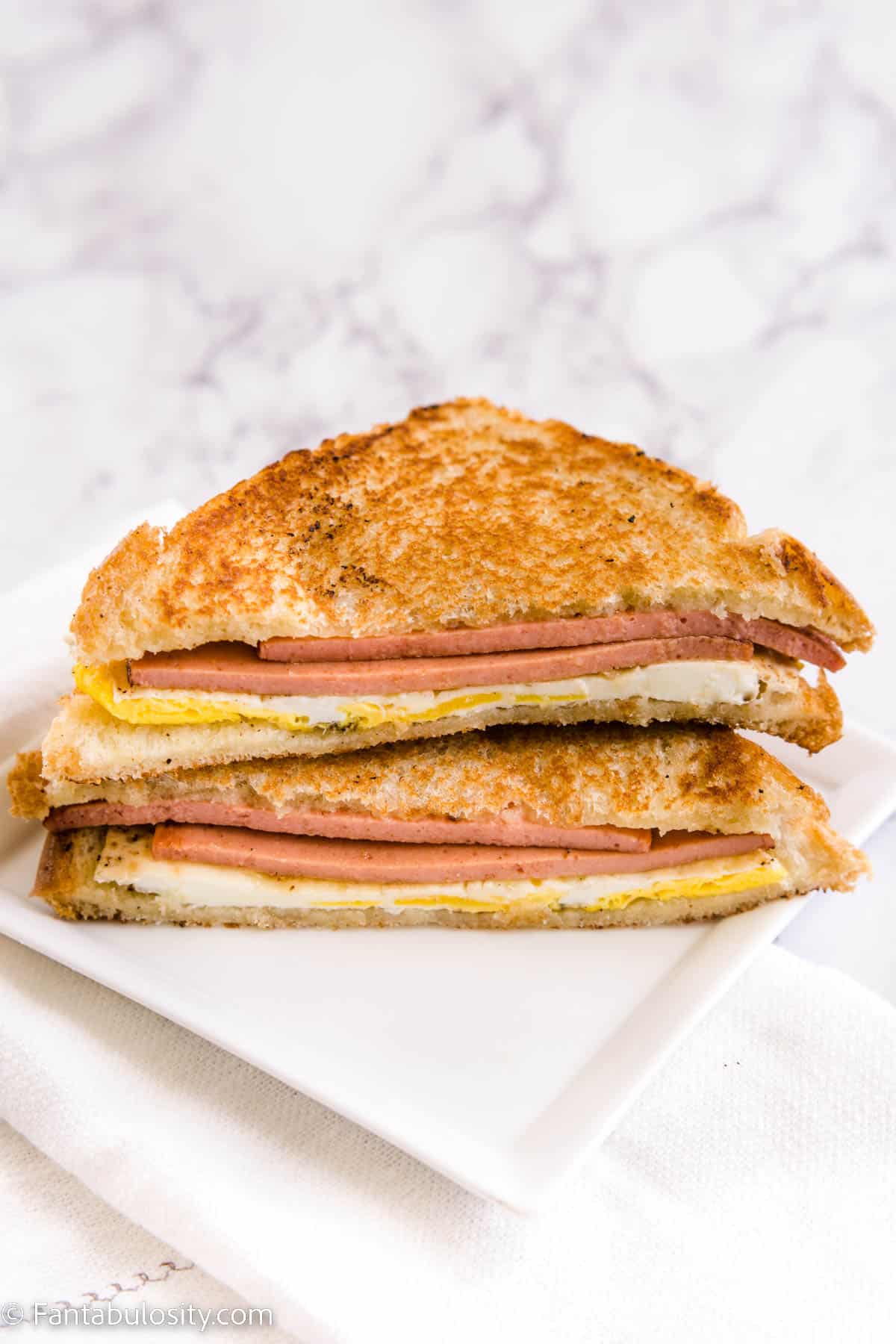 Fried bologna and egg sandwich cut in half on white plate