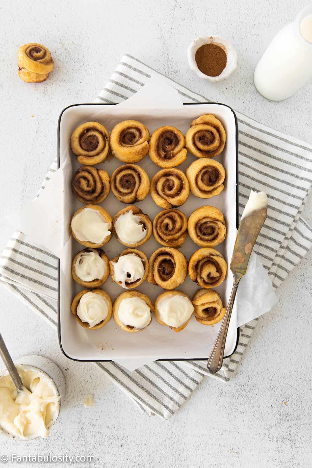 24 baked mini cinnamon rolls in a 9x13 baking dish with frosting on 7 of them.