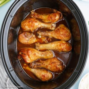 Eight cooked chicken drum sticks are swimming in a sauce in a black crock pot