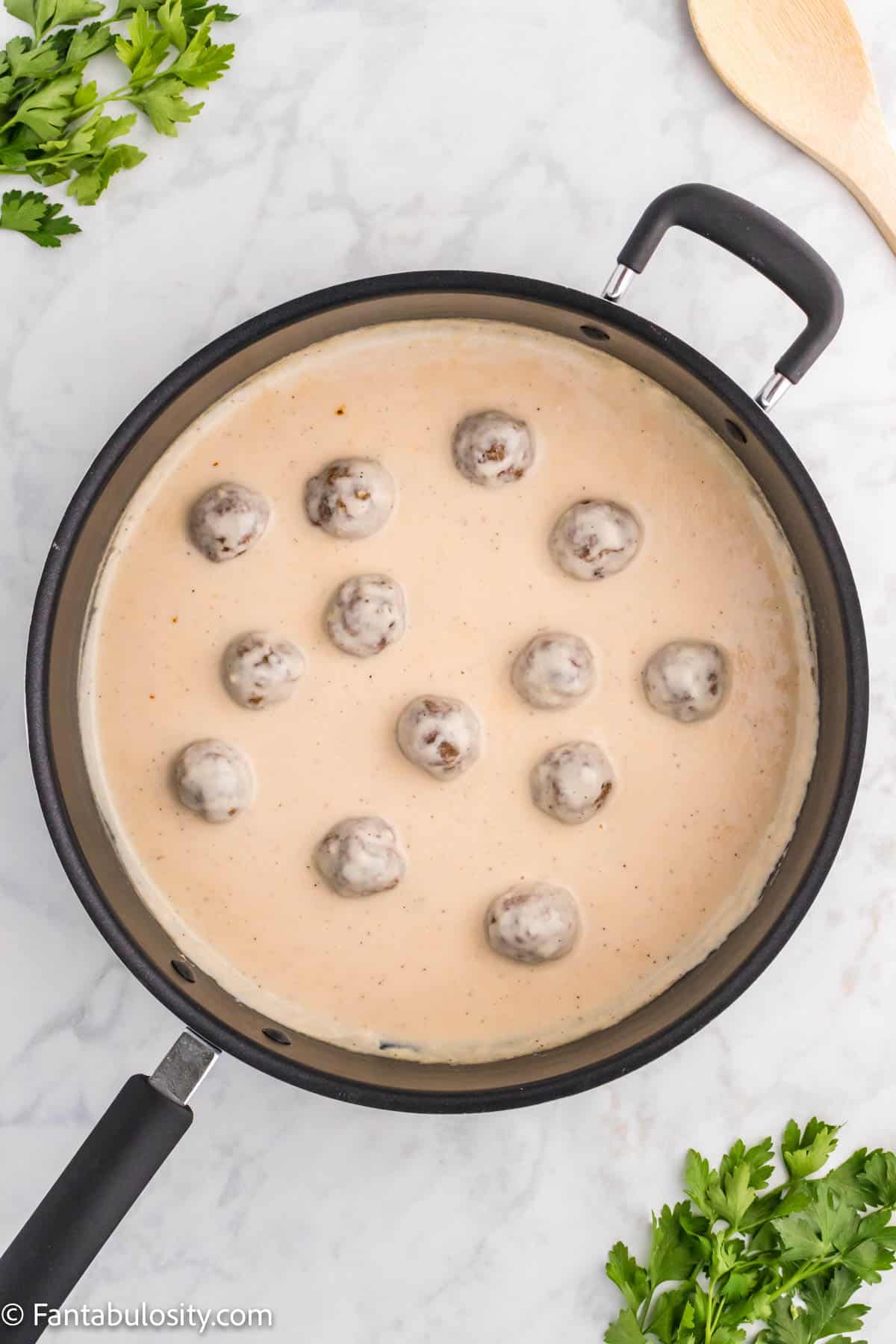 Cooked meatballs have been coated in thick creamy sauce and are simmering in a large black skillet