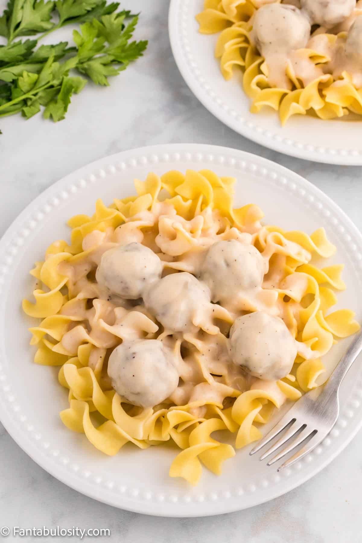 Swedish meatballs and sauce top cooked egg noodles on a white plate
