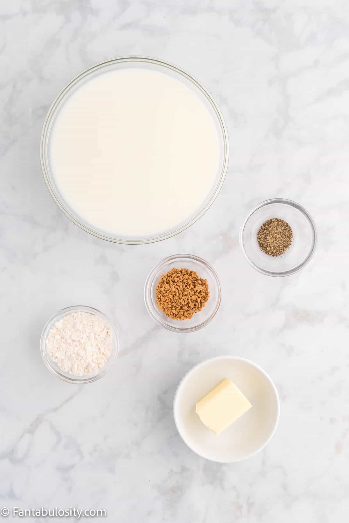 Milk, butter, flour and bowls of spices are displayed on a white marble background