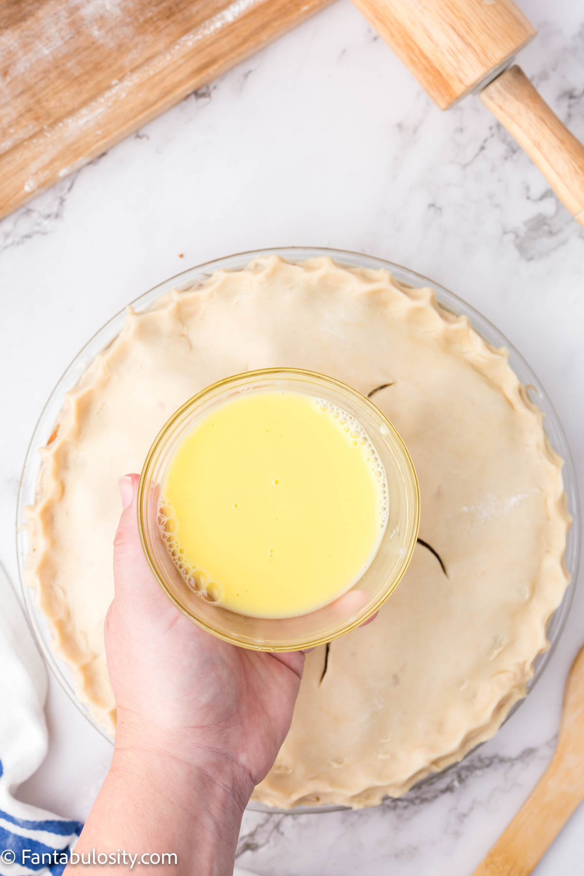 A small bowl of butter or egg white being held over an unbaked pie.