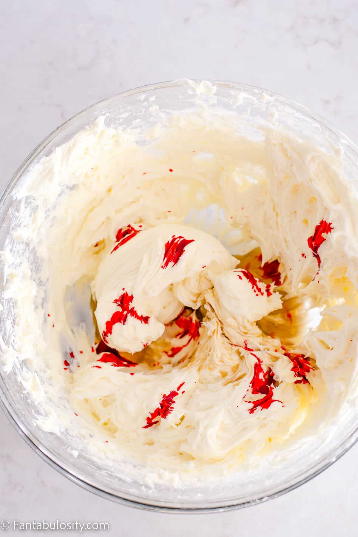Red food coloring drops in cream cheese mixture, in glass bowl