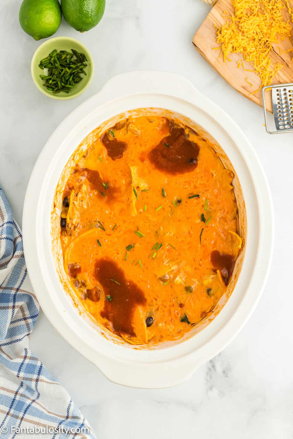 A slow cooker insert holds a crock pot chicken enchilada mixture topped with a layer of melty cheddar cheese