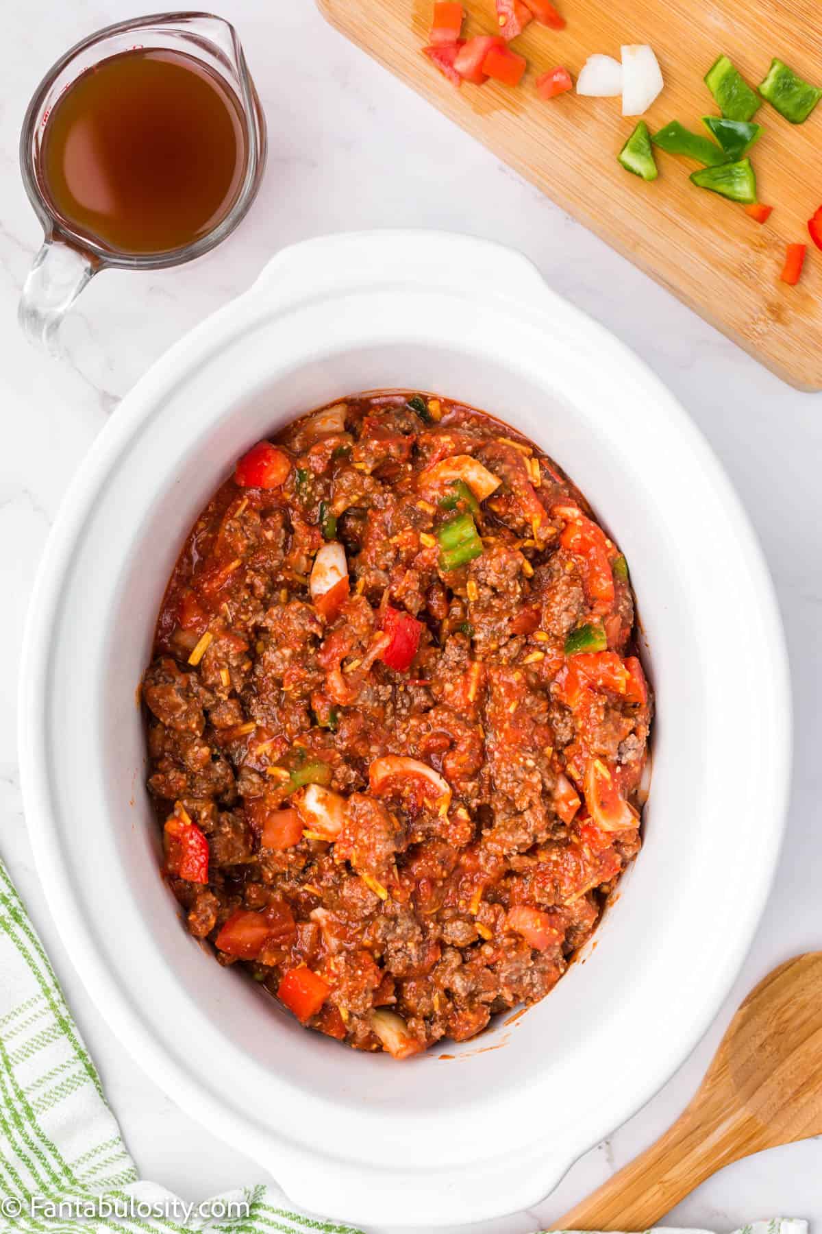 Beef broth is waiting to be added to a crock pot full of beef, vegetables, spices and cheeses in a rich tomato based sauce