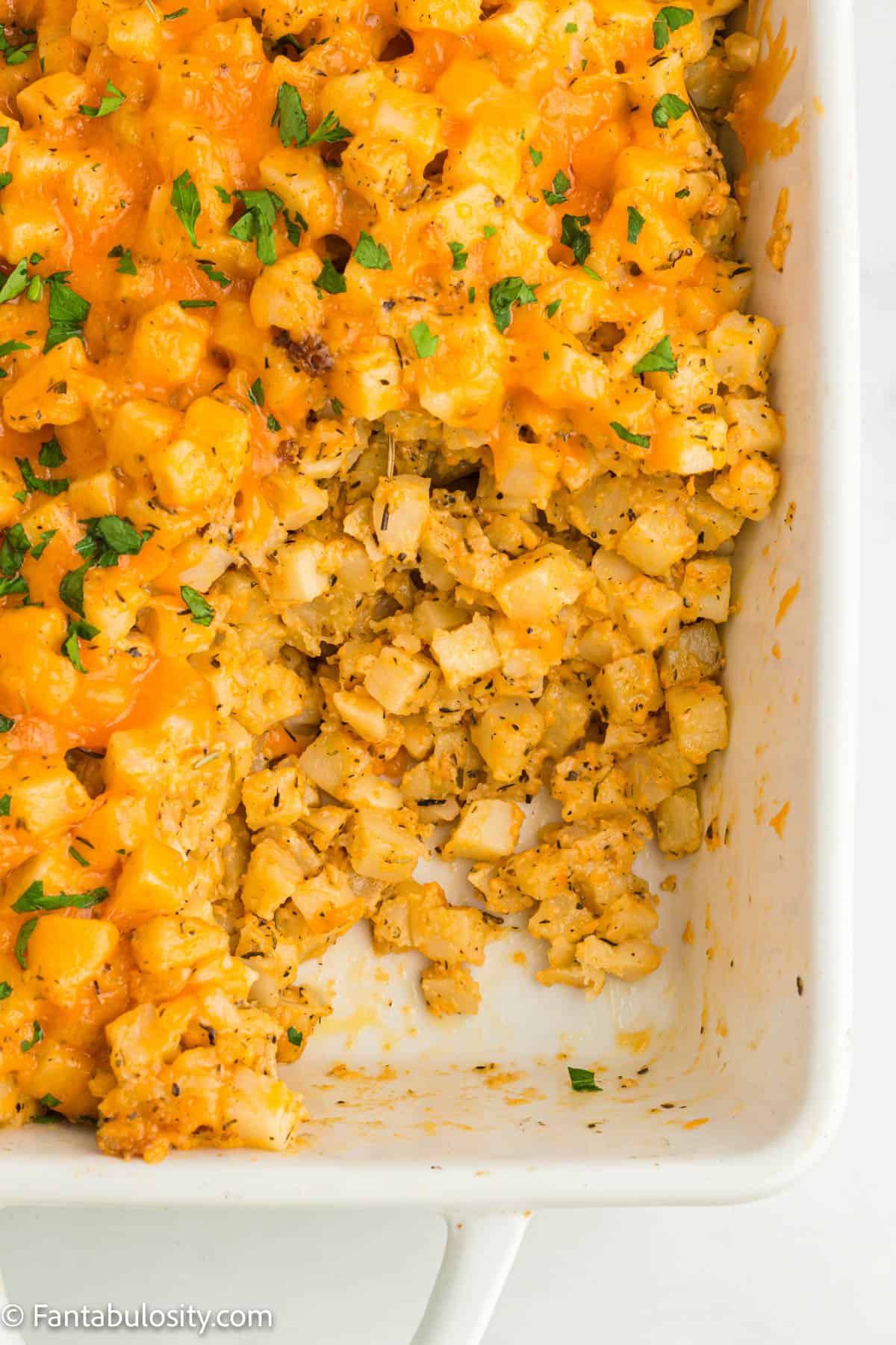 A few spoonfuls of cheesy hashbrown potatoes have been served from a white baking dish