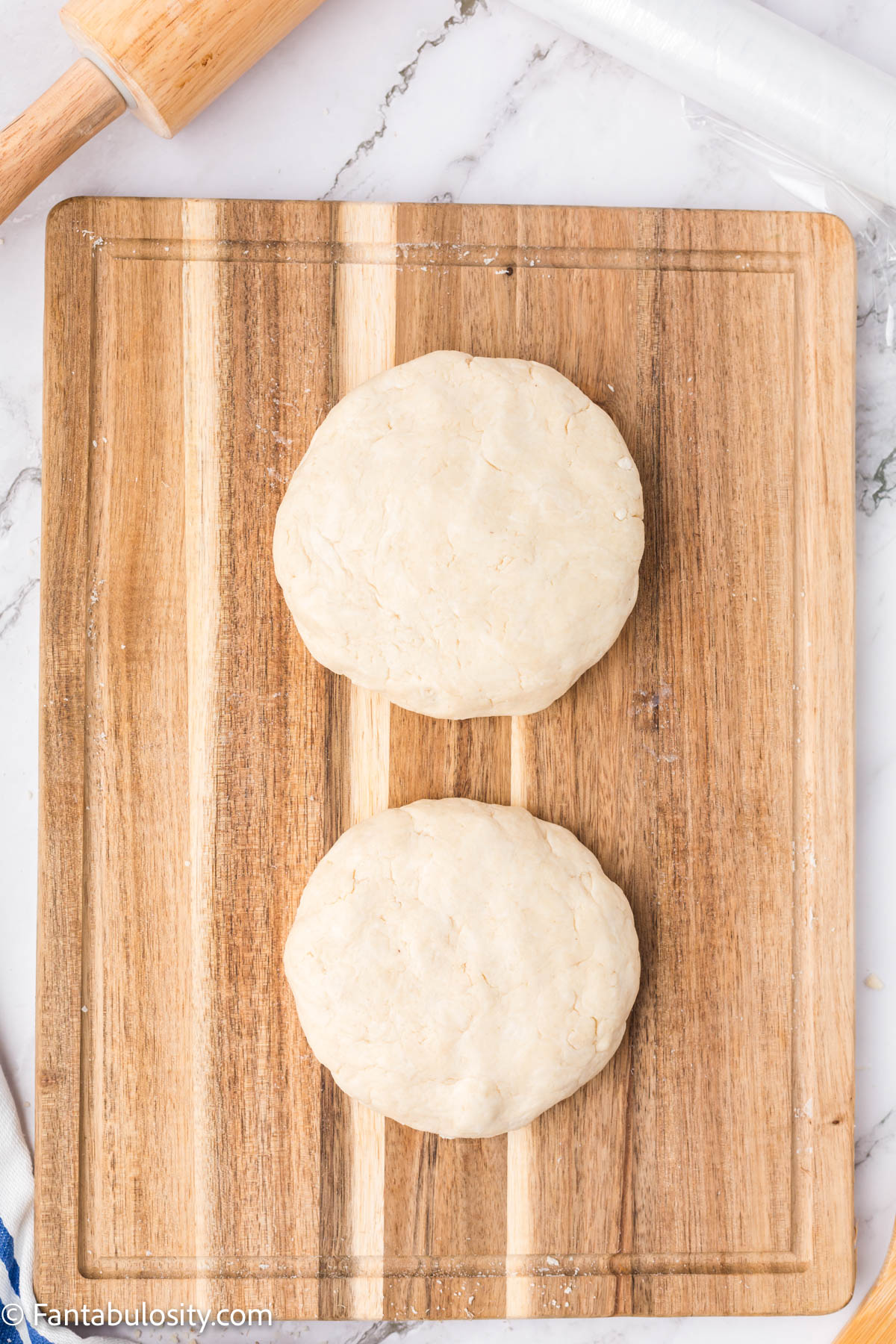 Two discs of dough on a wood cutting board. 