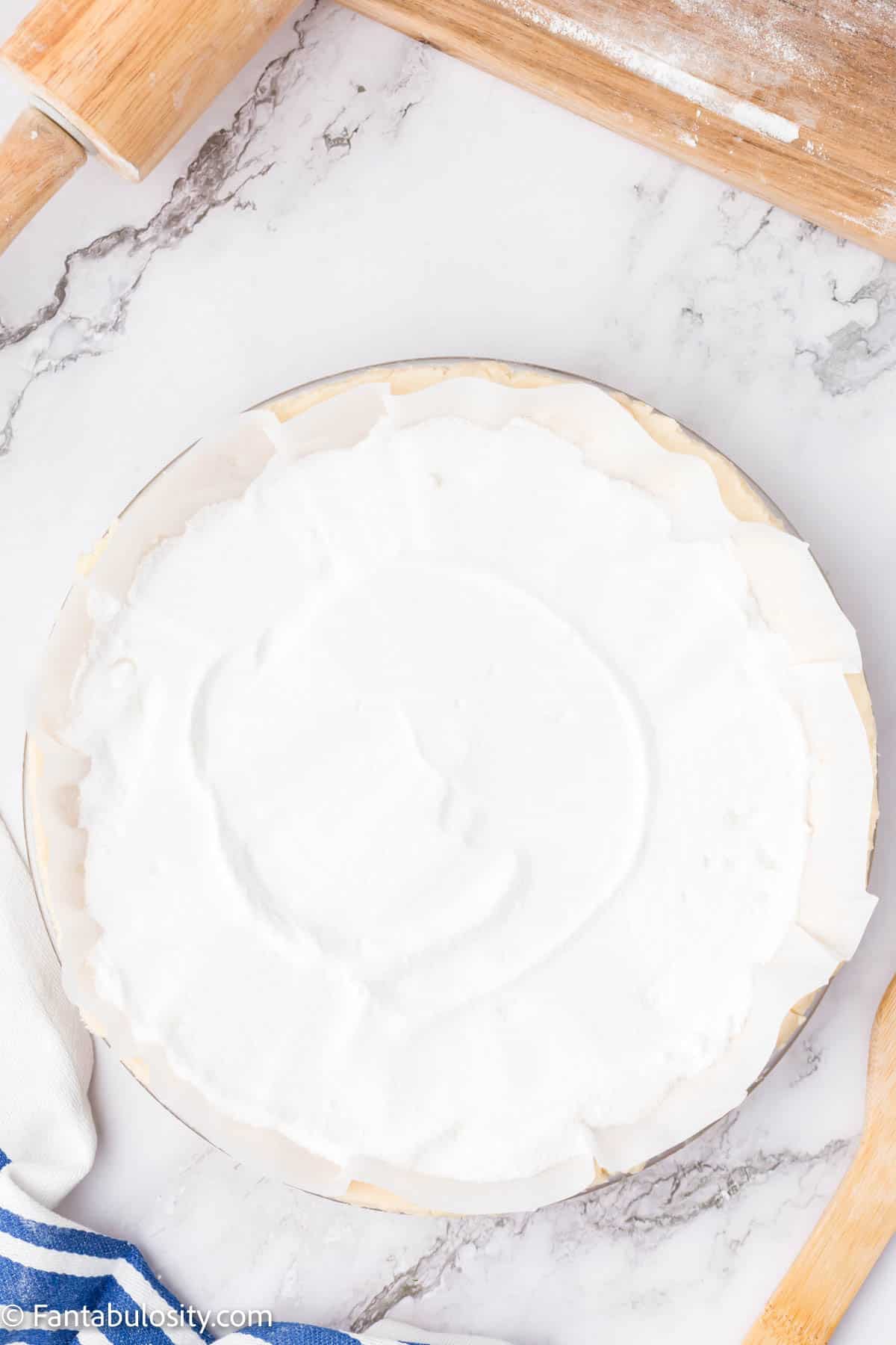 An unbaked pie crust covered with parchment paper and filled with sugar. 