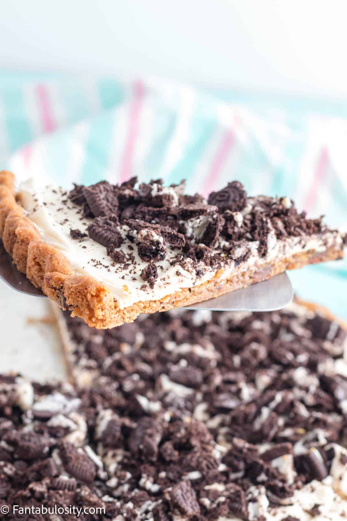 A metal spatula holds a slice of Oreo pizza above the dessert