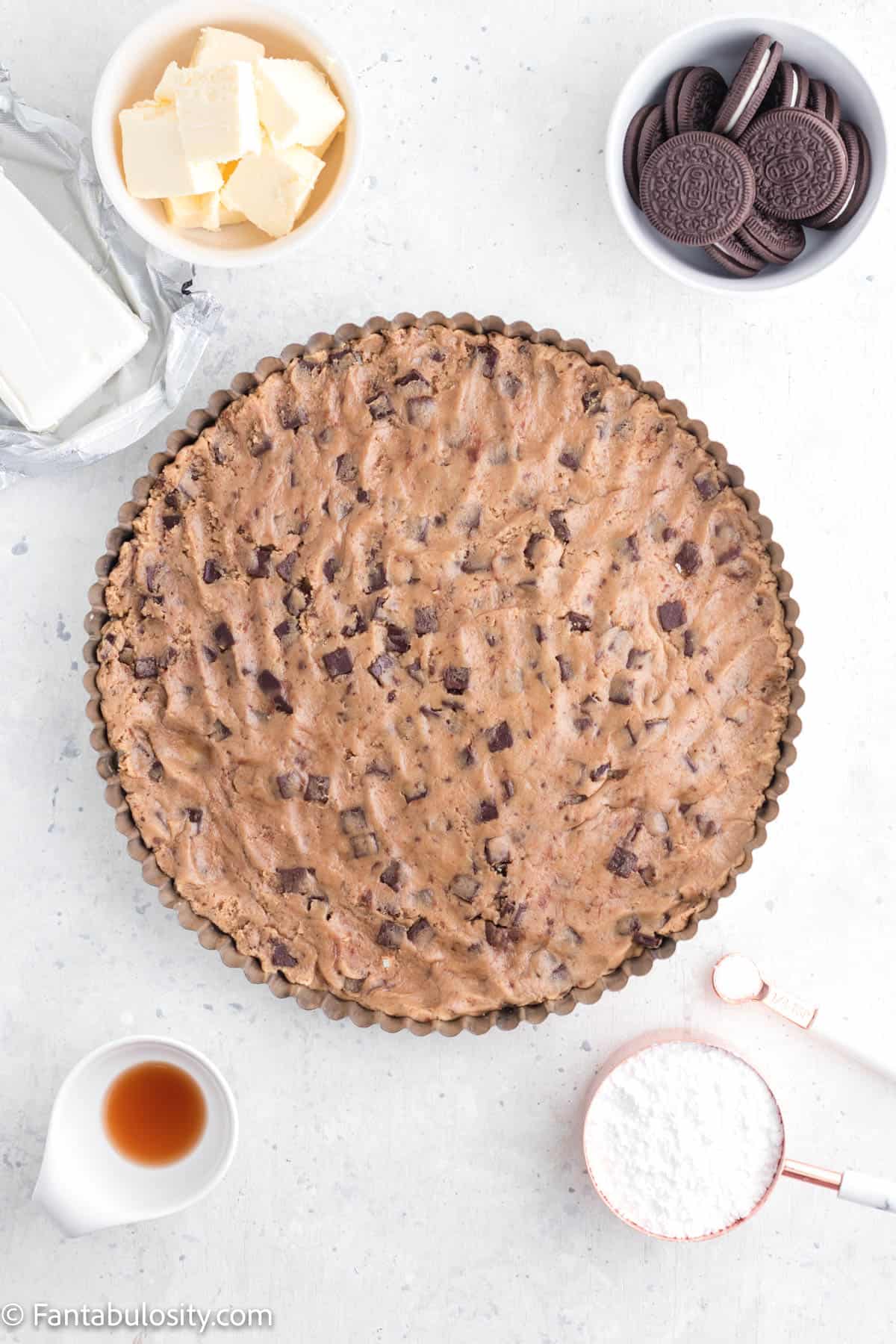 Chocolate chip cookie dough has been pressed into a 12 inch round tart pan and several other recipe ingredients are staged around it
