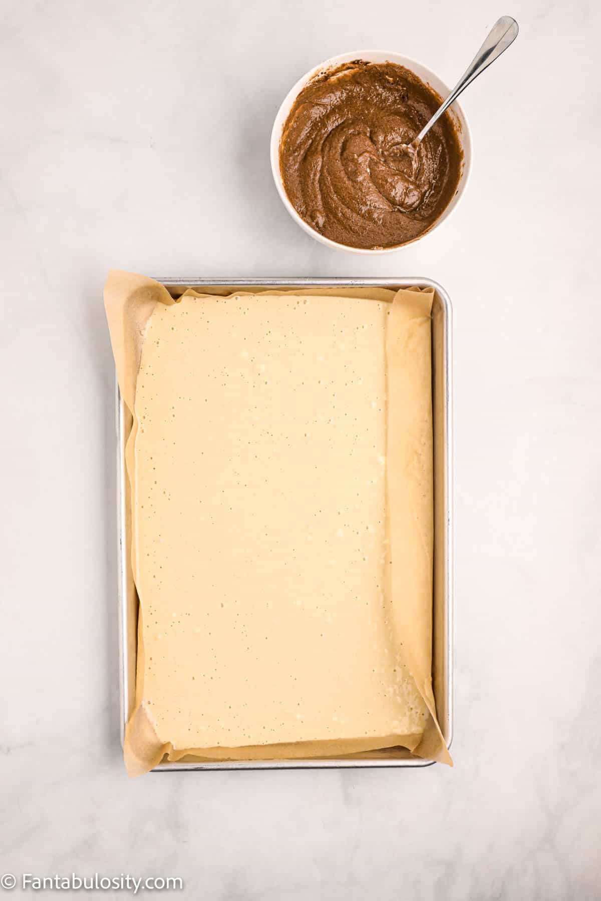A sheet pan of pancake batter waits for a brown sugar butter cinnamon sauce to be swirled in for sheet pan pancakes