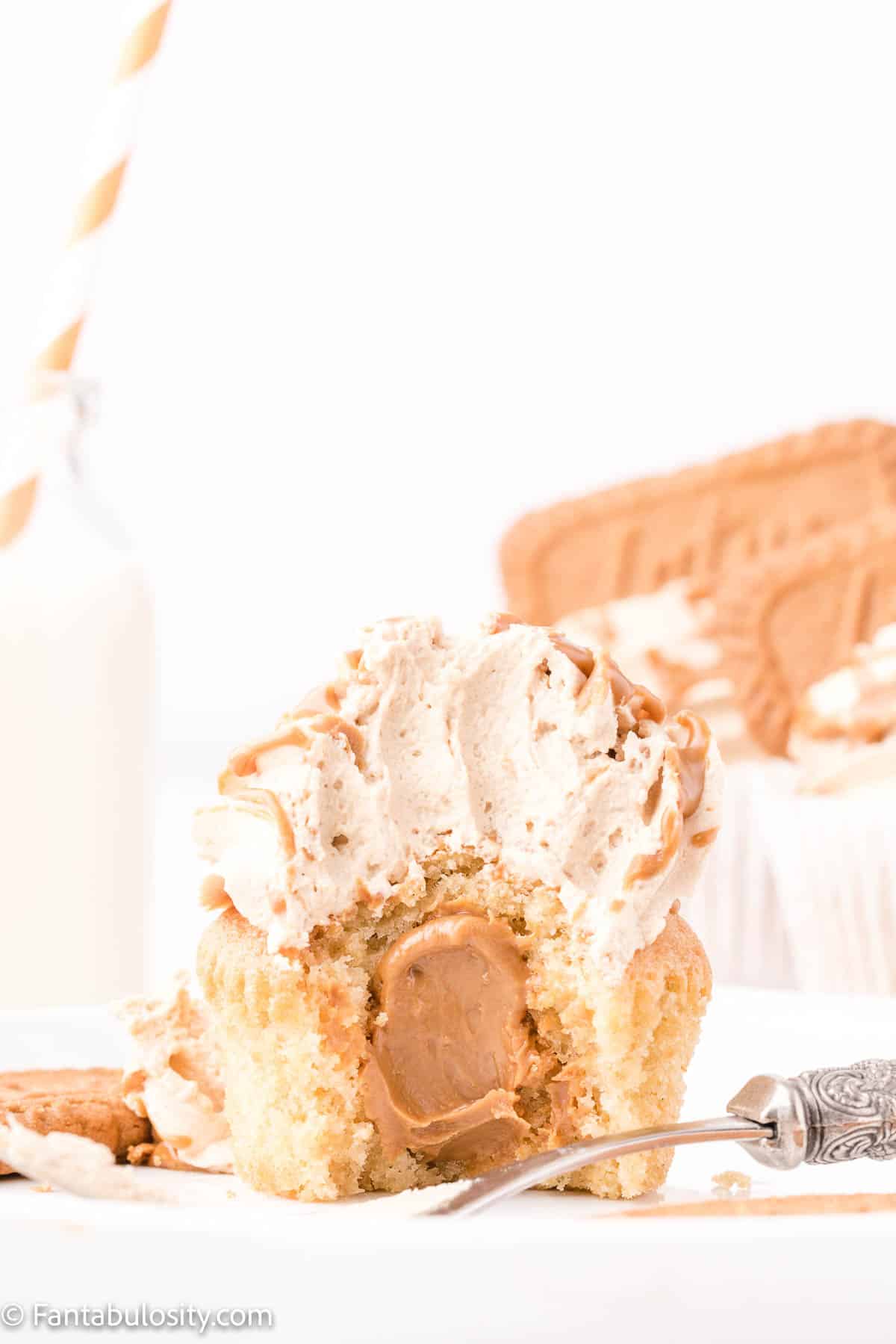 A frosted cupcake has been cut in half, revealing a center stuffed with Biscoff spread